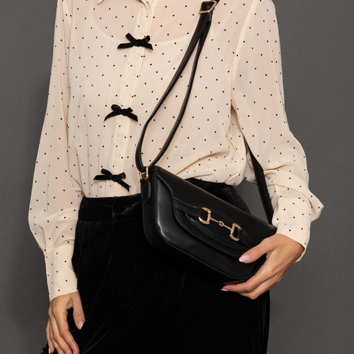 Person holding a black handbag with gold logo against a gray background