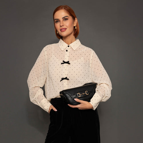 Woman wearing a white blouse with black buttons and holding a black handbag against a gray background
