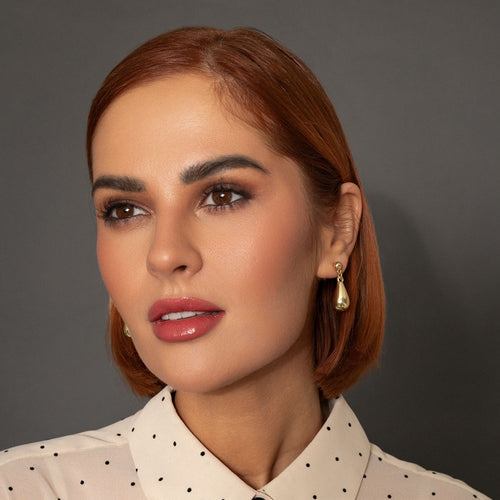 Close-up of a woman with red hair wearing a polka dot blouse against a gray background