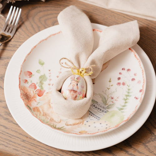 Decorative plate with floral design and folded napkin shaped like a bunny on a wooden table.