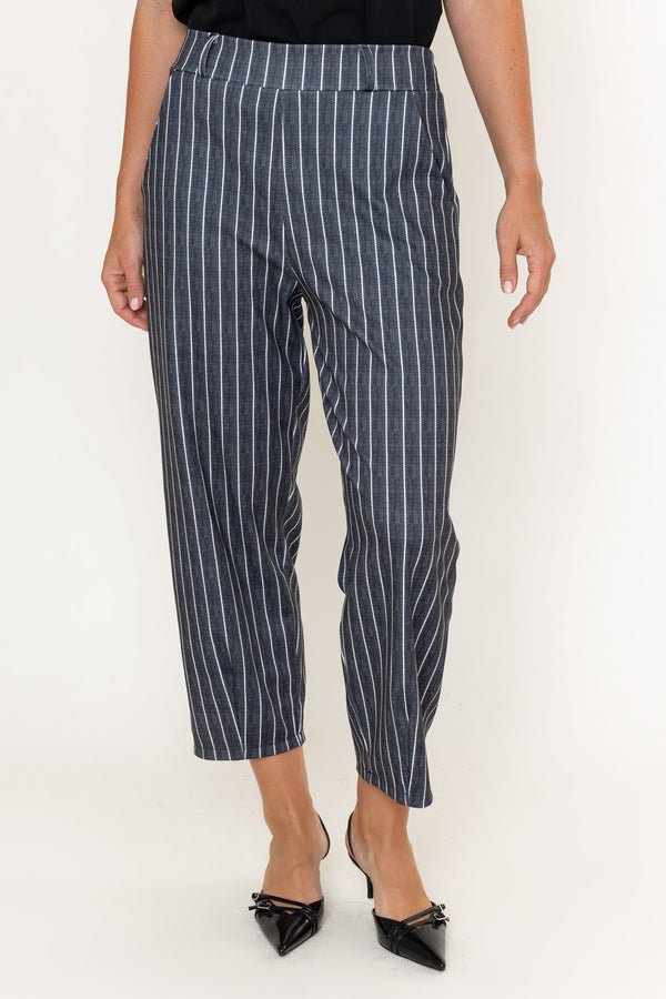 A model wearing navy blue cropped trousers with thin white vertical pinstripes, paired with black pointed-toe heels, shown from the waist down against a plain white studio background.