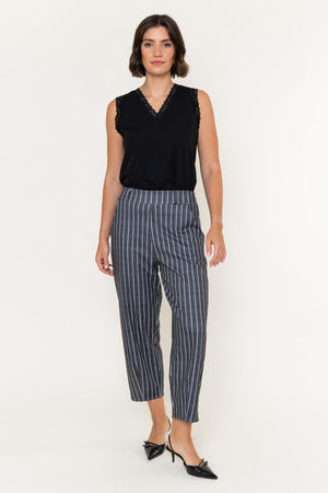 A woman modeling a sleeveless black top with lace trim and high-waisted navy pinstriped cropped trousers, paired with black pointed-toe heels, against a plain white studio background.