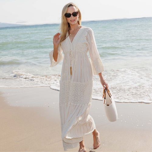 Woman in a white dress standing on a beach with ocean waves in the background