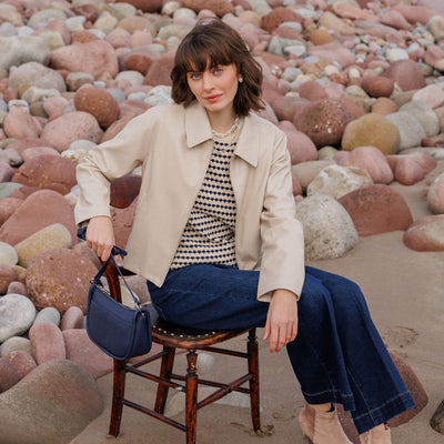 Woman sitting on a chair with a bag, surrounded by colorful rocks on a beach.