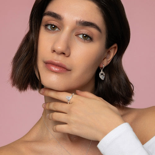 Woman wearing a diamond ring and earrings against a pink background