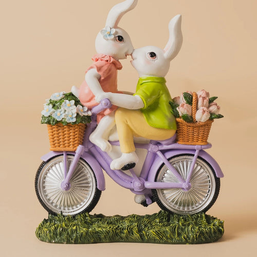 Two rabbits on a bicycle with flower baskets against a beige background