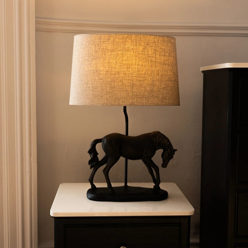 Table lamp with horse design on a marble surface against a neutral wall.