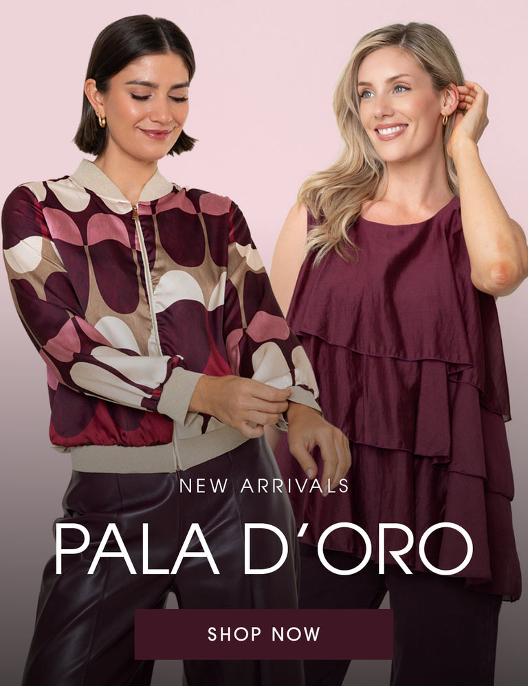 Two women modeling fashion apparel against a soft pink background, with large text reading 'NEW ARRIVALS PALA D'ORO' and a 'SHOP NOW' button. The left model wears a patterned satin jacket in burgundy, mauve, beige, and cream, paired with black leather pants.