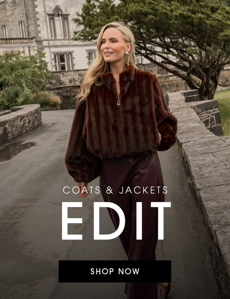 A woman stands outdoors wearing a dark brown faux-fur zip jacket and dark trousers, with a stone building and trees in the background. Large overlaid text reads 'COATS & JACKETS EDIT' and 'SHOP NOW'.