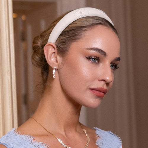 Woman wearing a white headband and earrings with a neutral background
