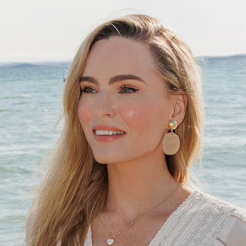 Woman with gold earrings and necklace against a beach background