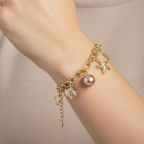 Gold bracelet with charms on a wrist against a neutral background