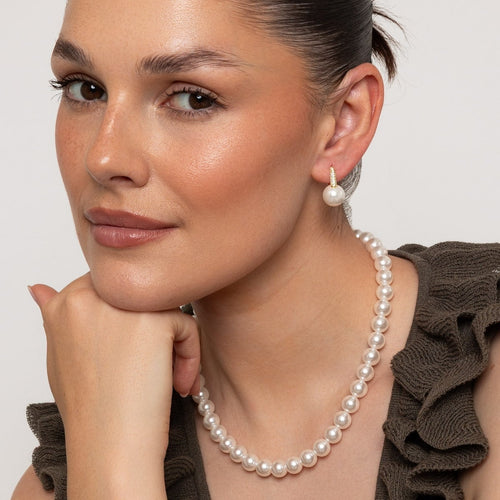 Woman wearing a pearl necklace and earrings against a neutral background